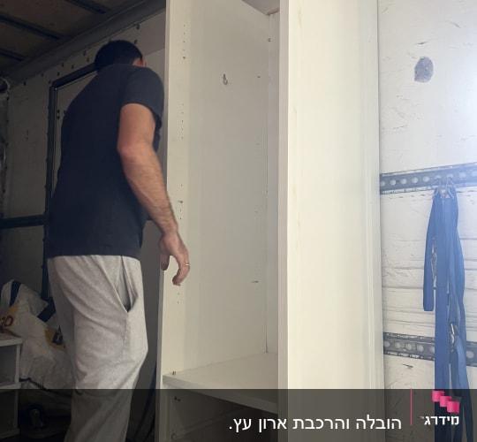 אדם מרכיב ארון לבן בתוך משאית הובלה